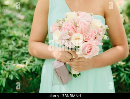 Eine Brautjungfer hält einen zarten Blumenstrauß in pastellfarbenen Blumen in einer lebendigen Gartenumgebung, während sie feiert. Stockfoto
