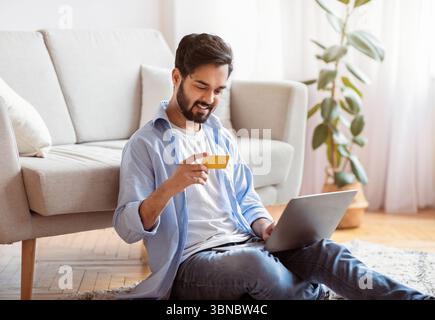 Millennial Arab Guy Macht Zahlungen Mit Laptop Und Kreditkarte Zu Hause Stockfoto