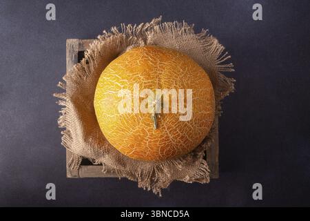 Melone liegt auf einer Leinenserviette in einer Holzkiste, auf dunklem Hintergrund, Blick von oben Stockfoto