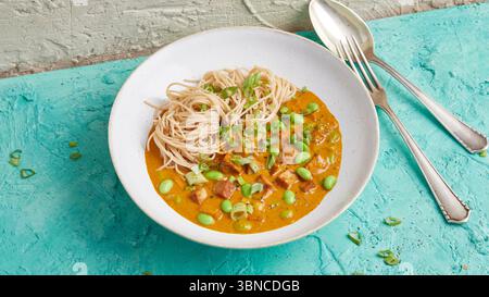 Warme Soba Nudelschale mit Tofu, cremiger Currysauce und Edamame – ein aromatisches Gericht auf pflanzlicher Basis, das asiatische Nudeln, Sojaprotein und Gemüse kombiniert. Stockfoto