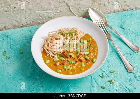 Warme Soba Nudelschale mit Tofu, cremiger Currysauce und Edamame – ein aromatisches Gericht auf pflanzlicher Basis, das asiatische Nudeln, Sojaprotein und Gemüse kombiniert. Stockfoto