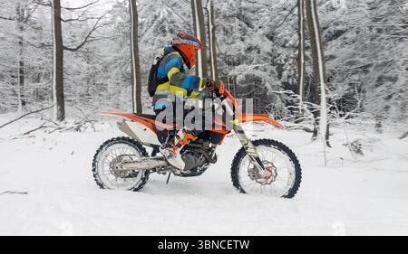 Ein Motorradfahrer navigiert mit einem Off-Road-Motorrad durch einen verschneiten Wald Stockfoto
