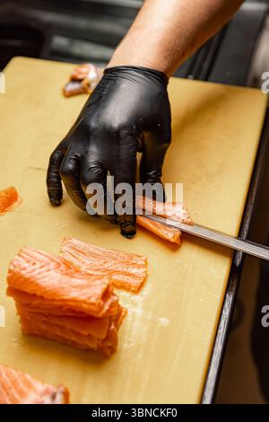 Handschuhe schneiden frischen Lachs auf einem Schneidebrett und bereiten Zutaten für eine köstliche Mahlzeit vor Stockfoto