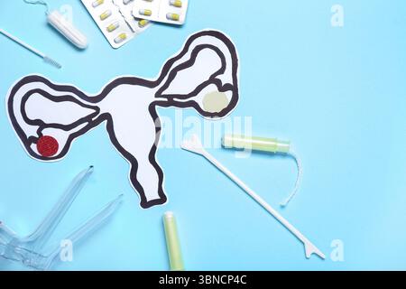 Papieruterus mit gynäkologischem Spekulum, Pillen und Tampons auf blauem Hintergrund Stockfoto