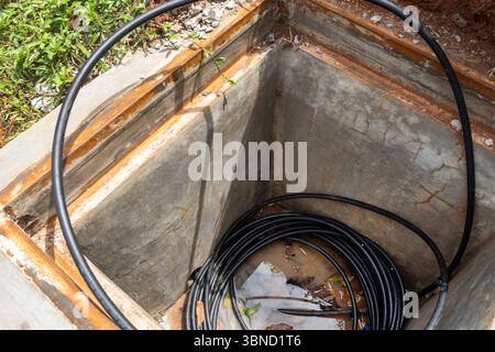Der schwarze Draht befindet sich in einem Loch im Boden. Der Draht ist von Wasser und Schmutz umgeben Stockfoto