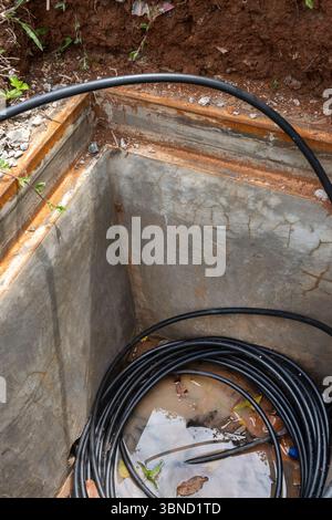 Der schwarze Draht befindet sich in einem Loch im Boden. Der Draht ist von Wasser und Schmutz umgeben Stockfoto