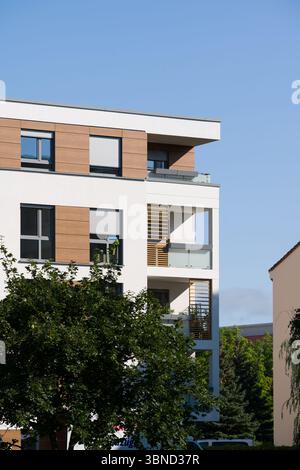 Außenecke eines modernen Apartmentgebäudes mit weißer Fassade, dekorativen Holzpaneelen und mehreren Balkonen. Die Balkone haben Glas Stockfoto