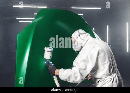 Arbeiter lackiert die Motorhaube in der Werkstattkammer mit einem Airbrush grün. Mann mit Spritzpistole beim automatischen Lackieren. Stockfoto