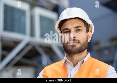 Ein Bauarbeiter, der einen Schutzhelm und eine Sicherheitsweste trägt, schaut mit ernstem Ausdruck direkt in die Kamera. Stockfoto