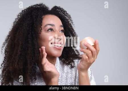 Schöne brasilianische Frau mit einem Glas Kollagencreme auf grauem Hintergrund Stockfoto