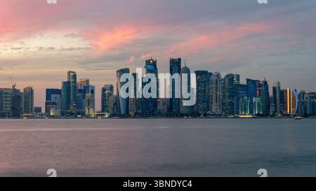 Panorama von Doha, der Hauptstadt von Katar. Blick auf Doha vom Meer. Wolkenkratzer auf rosa und blauem Hintergrund. Moderne Architektur von Doha bei Sonnenuntergang Stockfoto