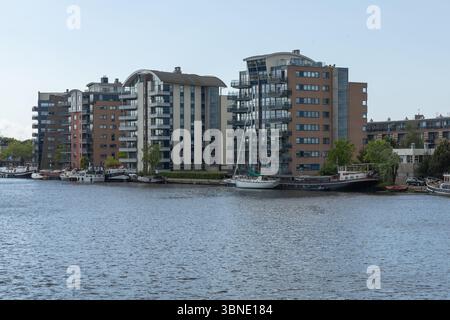 Diese zeitgenössische Küstenszene in Wormerveer, Niederlande, zeigt moderne Wohngebäude mit einzigartiger Architektur und Boote, die an der Küste liegen Stockfoto