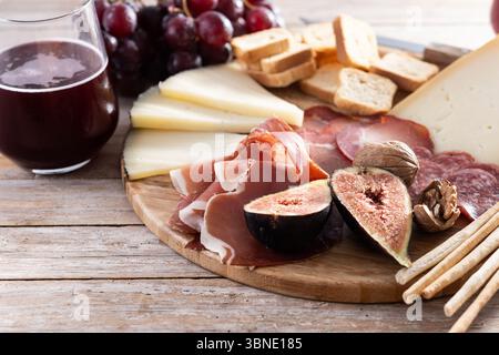 Eine rustikale Holzplatte mit verschiedenen Käsesorten, Wurstwaren, frischen Feigen, Walnüssen, roten Trauben, und Brotstäbchen Stockfoto