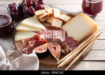 Eine rustikale Holzplatte mit verschiedenen Käsesorten, Wurstwaren, frischen Feigen, Walnüssen, roten Trauben, und Brotstäbchen Stockfoto