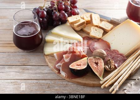 Eine rustikale Holzplatte mit verschiedenen Käsesorten, Wurstwaren, frischen Feigen, Walnüssen, roten Trauben, und Brotstäbchen Stockfoto