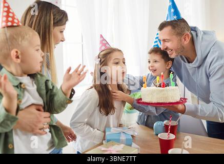 Fröhlich lächelnde Familie feiert den Geburtstag der Tochter als glückliches Mädchen, das Kerzen auf dem Kuchen ausbläst. Stockfoto