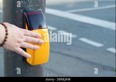 Eine Hand greift aktiv mit einer hellgelben Fußgängertaste ein, die sich an einem Straßenmast in der Nähe des Verkehrs befindet Stockfoto