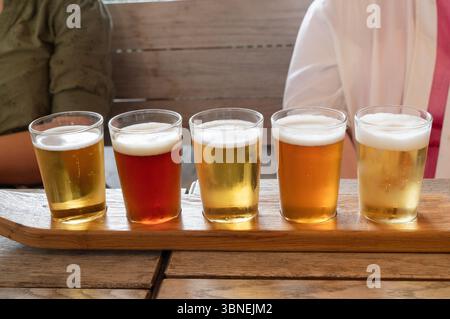 Eine kuratierte Auswahl an verschiedenen Craft-Bieren mit verschiedenen Stilen, die in einem eleganten Holzflug serviert werden Stockfoto