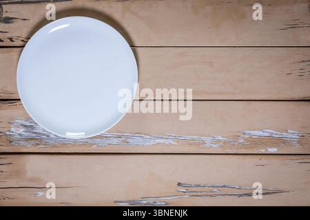 Von oben nach unten auf eine weiße Porzellanplatte in der oberen linken Ecke auf einem alten beigefarbenen Holztisch mit abblätternder Farbe. Der Rest des Rahmens ist leer. Stockfoto