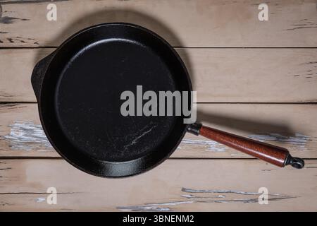 Ansicht von oben auf eine große gusseiserne Pfanne mit Holzgriff, der den gesamten Rahmen ausfüllt, zeigt Materialstruktur und dunkle Kochfläche. Stockfoto
