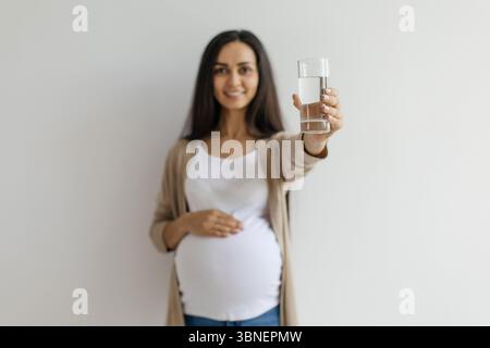 Schwangere Frau lächelt und bietet ein Glas Wasser zur Kamera Stockfoto