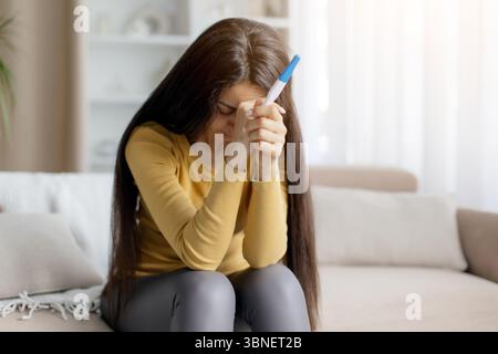 Depressive Frau, die einen Schwangerschaftstest in beiden Händen hält und weint Stockfoto
