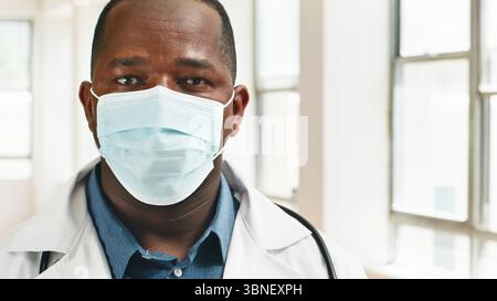 Medizinischer Fachmann mit Schutzmaske im sonnendurchfluteten Krankenhauskorridor Stockfoto