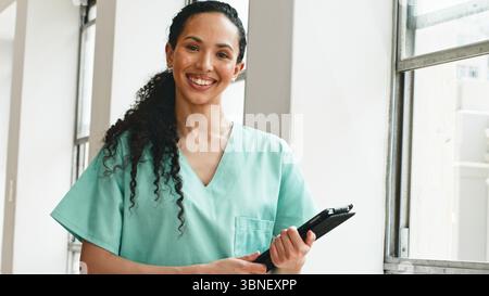 Freundlicher Healthcare-Mitarbeiter lächelnd in Uniform hält Clipboard in heller medizinischer Einrichtung Stockfoto