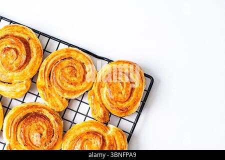 Blätterteigbrötchen, Brötchen oder Schnecken mit Zucker und Zimt auf einem schwarzen Drahtgestell auf weißem Hintergrund. Kopierraum. Hochwertige Fotos Stockfoto