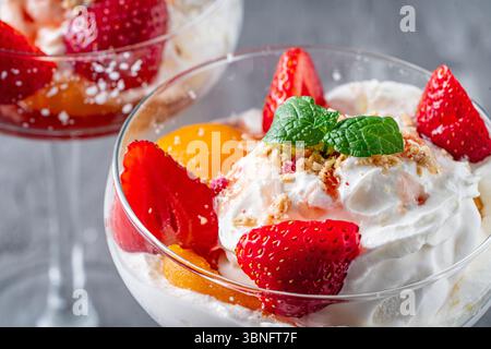 Eis mit Schlagsahne, Erdbeeren und Pfirsich in einem Glas auf grauem Hintergrund. Nahaufnahme. Hochwertige Fotos Stockfoto