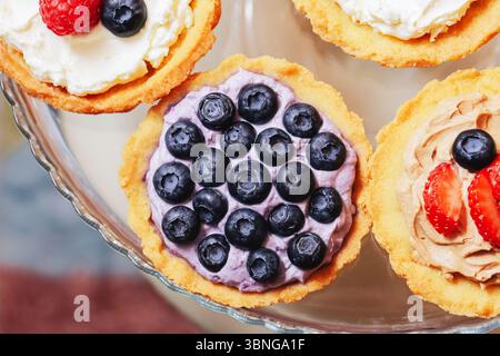 Bunte Beerentörtchen. Mini-Obstkuchen mit Heidelbeeren und Erdbeeren. Köstliches Dessert auf Glasplatte. Süßes Gebäck im Sommer. Hausgemachter Gourmet. Stockfoto