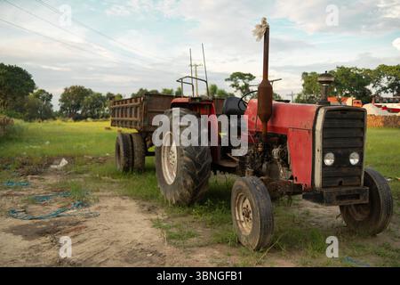 Ein roter Traktor mit einem Anhänger, der auf einem Feld geparkt ist Stockfoto