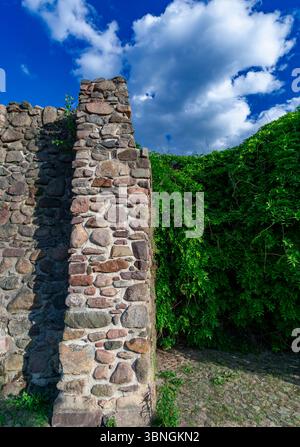 Vertikales Bild einer historischen Steinmauer, die mit Efeu bewachsen ist, vor einem leuchtend blauen Himmel mit flauschigen Wolken an einem Sommertag. Stockfoto