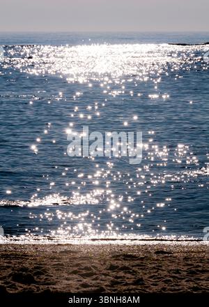 Das Bild zeigt einen Wasserkörper mit Sonnenlicht, das von der Oberfläche reflektiert wird. Das Wasser hat eine tiefblaue Farbe, und das Sonnenlicht erzeugt einen funkelnden Effekt. Stockfoto