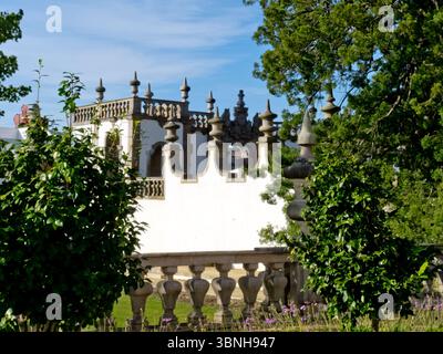 Blick auf eine weiße Wand mit dekorativen Elementen, eingerahmt von Bäumen und Laub, unter blauem Himmel. Stockfoto