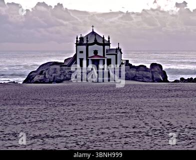 Eine Kapelle befindet sich auf einem Felsvorsprung am Strand, mit dem Ozean und dem bewölkten Himmel im Hintergrund. Stockfoto