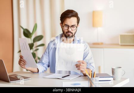 Handsome Eastern Entrepreneur Lesen Von Finanzpapieren, Während Sie Am Schreibtisch Sitzen Im Büro Stockfoto