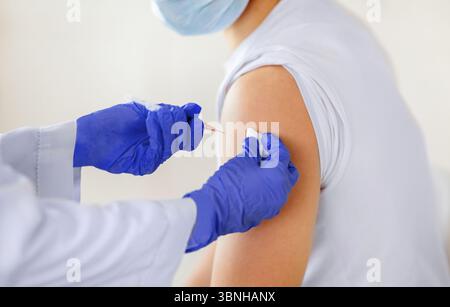 Beschnittene Ansicht eines jungen männlichen Patienten, der in der Klinik eine Injektion mit Coronavirus-Impfstoff erhalten hat, Nahaufnahme Stockfoto
