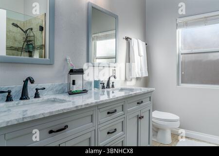 Graues Badezimmer mit Doppelwaschbecken, Marmorspiegel, Schrank, Armaturen, Handtüchern und Toilette Stockfoto