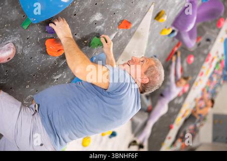 Der ältere Mann klettert ohne Seile und Gurte an der Boulderwand Stockfoto