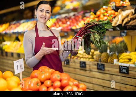 Die weibliche Mitarbeiterin im Lebensmittelgeschäft bietet reife Rüben in der Lebensmittelabteilung des Supermarktes an Stockfoto