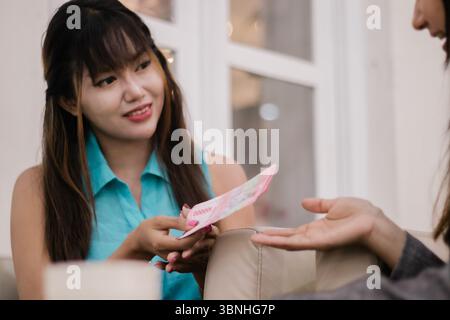 Zwei Frauen führen eine Finanztransaktion durch. Man überreicht gerne indonesische Rupiah-Banknoten. Ein Symbol für Handel, Schulden oder finanzielle Inter Stockfoto