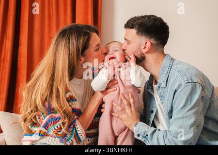 Dieses wunderschöne Bild zeigt die herzerwärmenden Momente liebevoller Eltern, die ihr fröhliches Baby küssen, und zeigt das pure Wesen der Familie Stockfoto