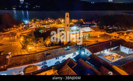 Ein atemberaubender Blick aus der Luft auf Guatavita, Kolumbien bei Nacht, mit beleuchteten Gebäuden und der malerischen Laguna de Guatavita im Hintergrund. Stockfoto