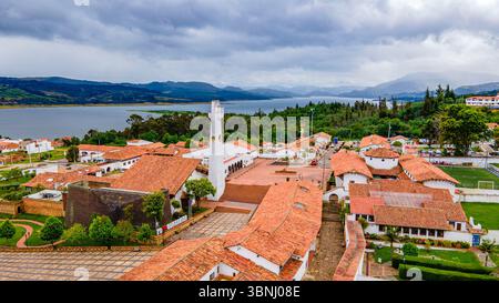Atemberaubende Aussicht auf Guatavita, Kolumbien, mit der berühmten Laguna de Guatavita und traditionellen roten Ziegeldächern inmitten üppiger Vegetation. Stockfoto