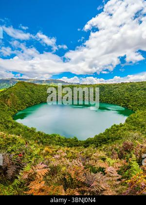 Atemberaubender Panoramablick auf die Laguna de Guatavita, umgeben von üppigem Grün und blauem Himmel, die Kolumbiens natürliche Schönheit zeigt. Stockfoto
