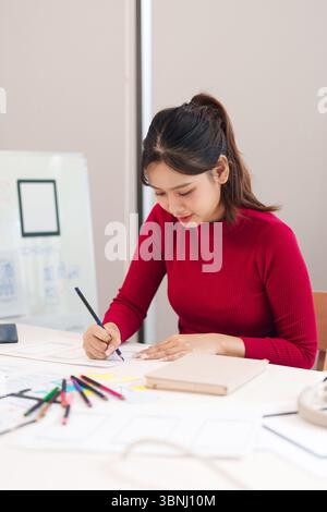 Eine junge asiatische Frau skizziert Benutzeroberflächenlayouts auf Papier. Sie entwirft eine Website und eine mobile App für ihr Startup. Erstellen einer Benutzererfahrung f Stockfoto