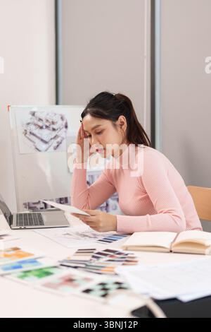 Dieses Bild zeigt eine junge Erwachsene asiatische Frau UI UX-Designerin, die an einem Designprojekt an ihrem Schreibtisch arbeitet. Sie ist aufgrund fehlender kreativer Ideen gestresst. Stockfoto