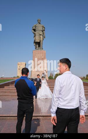 Eine typische Szene einer Hochzeitsfeier, die Fotos macht. An der riesigen Skulptur Amir Timur, Statue des Führers in Shahrisabz, Usbekistan. Stockfoto