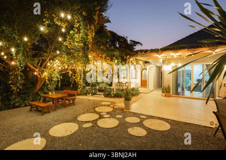 Tropischer Garten mit Koi-Teich und gemütlicher hölzerner Terrasse, Ein üppiger tropischer Garten mit lebhaftem Laub und ein ruhiger Koi-Teich befindet sich vor einem gemütlichen Stockfoto